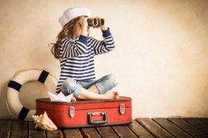 Girl sitting on suitcase looking to the distance with binoculars