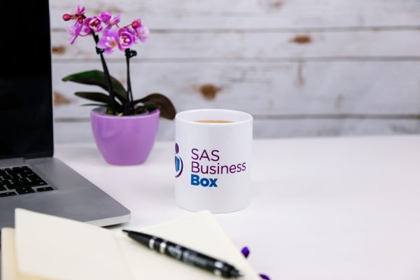 Mug with SAS business box logo next to pen and laptop