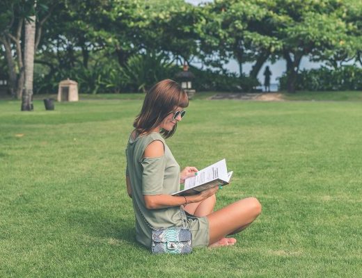 Woman reading book whilst sitting outside on grass